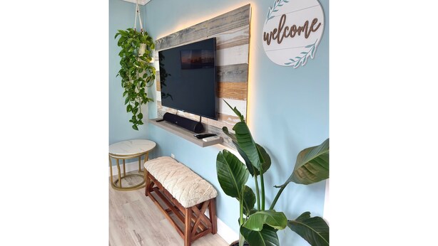 Ein Zimmer mit an der Holzwand befestigtem Fernseher, einem runden Tisch mit einer Bank und einem 'welcome'-Schild.