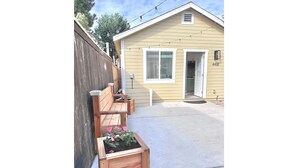 Ein Haus mit Holzzaun, einer Beton-Terrasse und einem Holz-Pflanzkasten mit rosa Blumen.