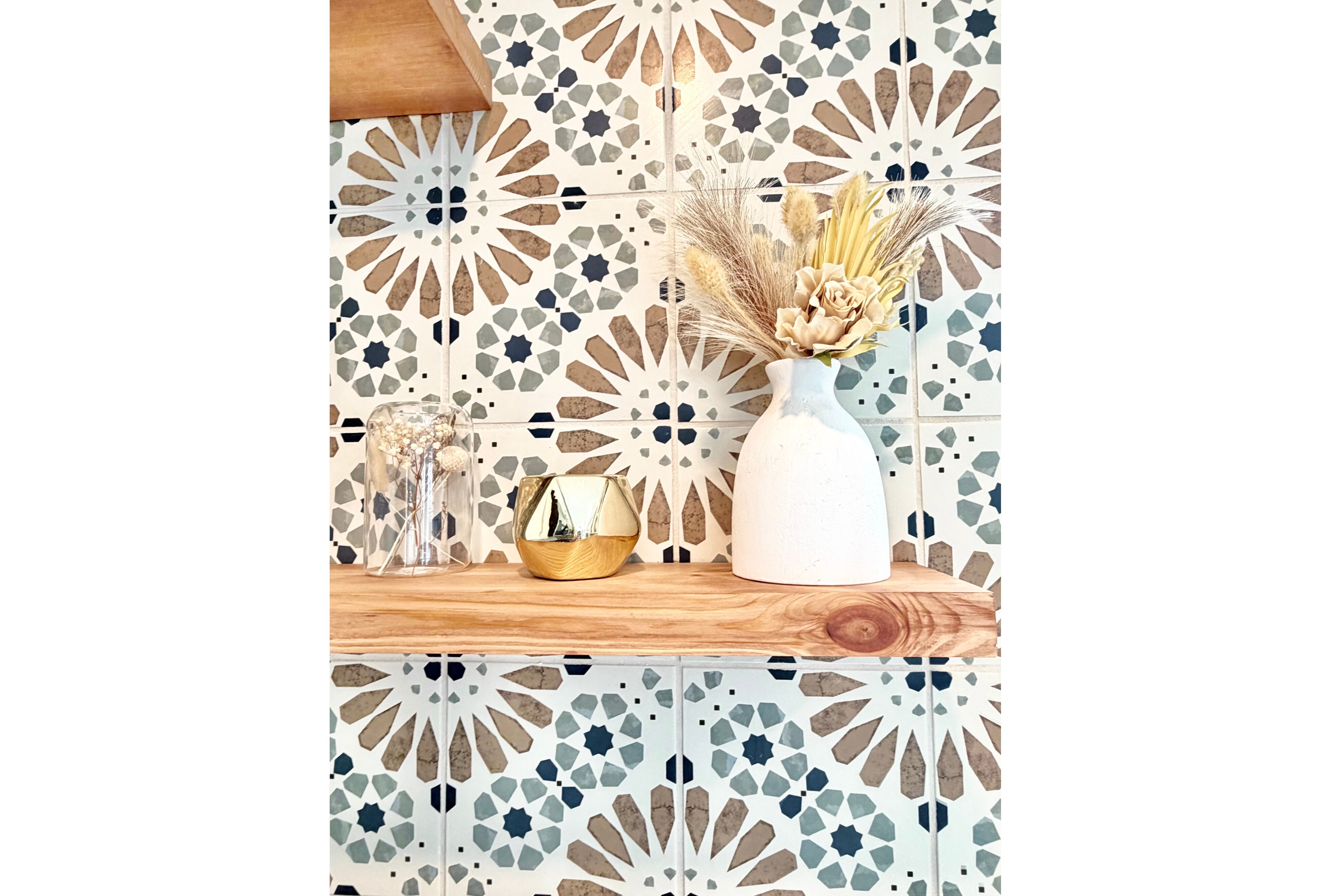 Une étagère sur laquelle se trouvent un vase blanc contenant des fleurs séchées, un petit bol doré et un récipient en verre transparent renfermant un objet décoratif.
