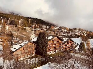 Uma cidade montanhosa com edifícios cobertos de neve, incluindo um hotel imponente de vários andares com varandas.