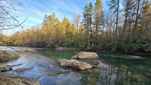 Ein klarer Fluss mit Steinen und Bäumen im Hintergrund.