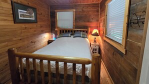 Ein Schlafzimmer in einer Holzhütte mit einem Bett, einer Nachttischlampe und einem gerahmten Bild an der Wand.