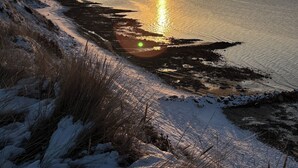 Vista d'un capvespre a la costa amb paisatge cobert de neu i mar tranquil·la.