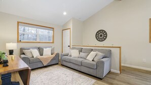 Ein Wohnzimmer mit zwei grauen Sofas, einem Holztisch, einem gemusterten Teppich und einer Wanddekoration.