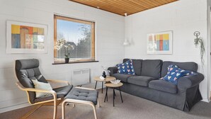 A modern living room with a grey sofa, a wooden-framed armchair, a small round table, and a potted plant. - Cosy holiday home for 6 near beach/sea (Sydals)