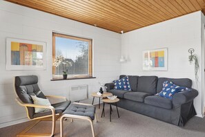 A modern living room with a grey sofa, a wooden-framed armchair, a small round table, and a potted plant. - Cosy holiday home for 6 near beach/sea (Sydals)