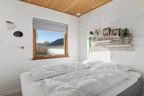 Ein Schlafzimmer mit einem Bett, einem Fenster, einem Wandregal mit Dekoration und einer Holzbalkendecke.