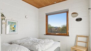A bedroom with a bed, a wooden chair, a window with a view, and a wall-mounted artwork. - Cosy holiday home for 6 near beach/sea (Sydals)