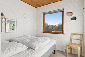 A bedroom with a bed, a wooden chair, a window with a view, and a wall-mounted artwork. - Cosy holiday home for 6 near beach/sea (Sydals)