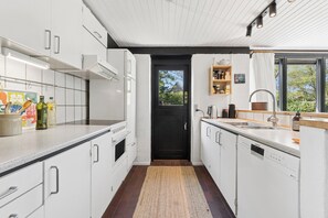 A modern kitchen with white cabinetry, a black door, and a view through the window. - Lovely holiday home near the water (Hurup Thy)