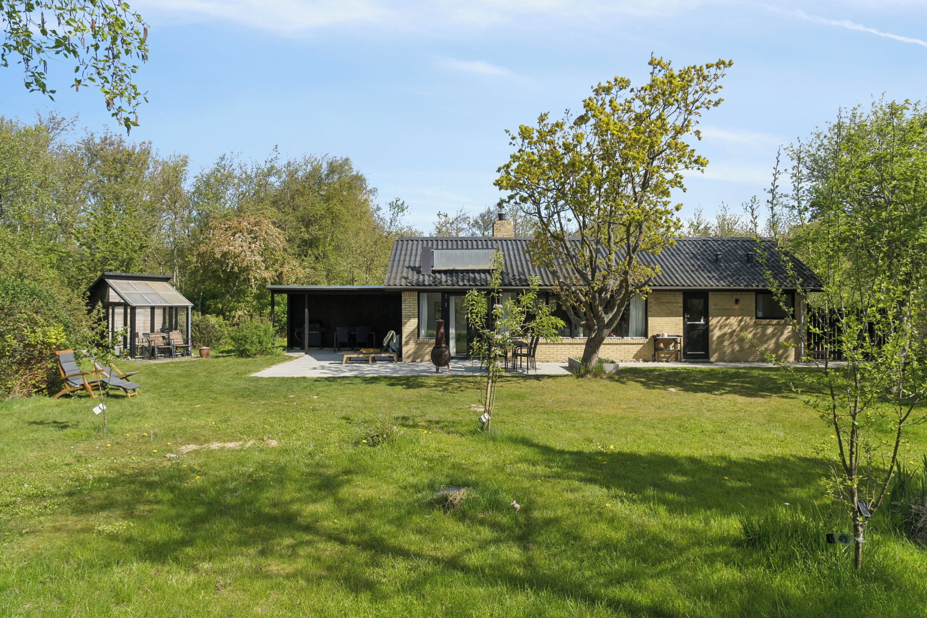 A modern house with a patio, a small detached structure, and a well-maintained lawn.