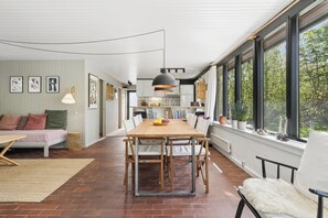 A modern kitchen with a dining table, chairs, and a large window overlooking greenery. - Lovely holiday home near the water (Hurup Thy)