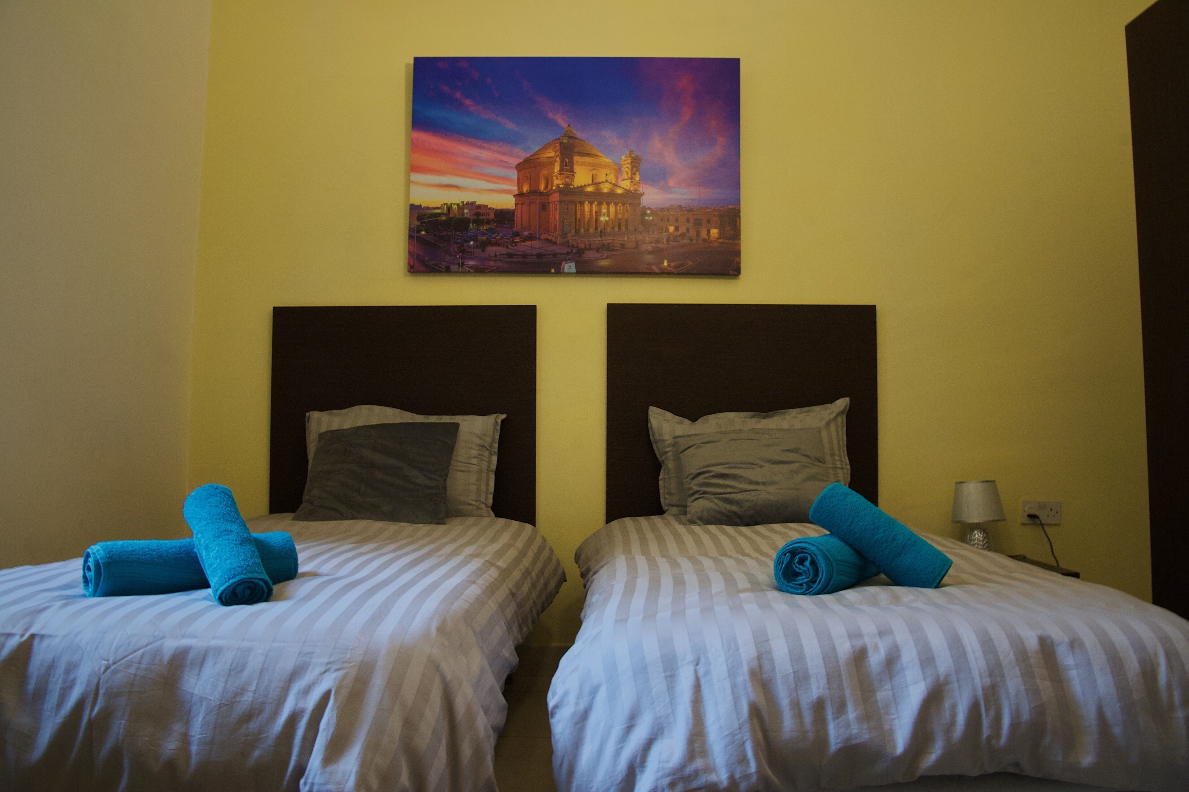 A hotel room with two beds, each with a pillow and a rolled towel.