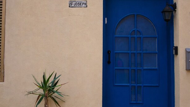 Un edificio con puerta azul, un letrero que dice “S Joseph” y una planta en maceta a su lado.