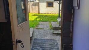 A doorway leading to a backyard with a concrete path, a small window, and a metal grate. - East Vancouver Bachelor Basement Suite. Pet Friendly - No Fee. Next to Transit. (Vancouver)