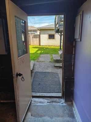 A doorway leading to a backyard with a concrete path, a small window, and a metal grate. - Spacious Bachelor Basement Suite of Historic Old Home. Pet Friendly. Cable TV (Vancouver)