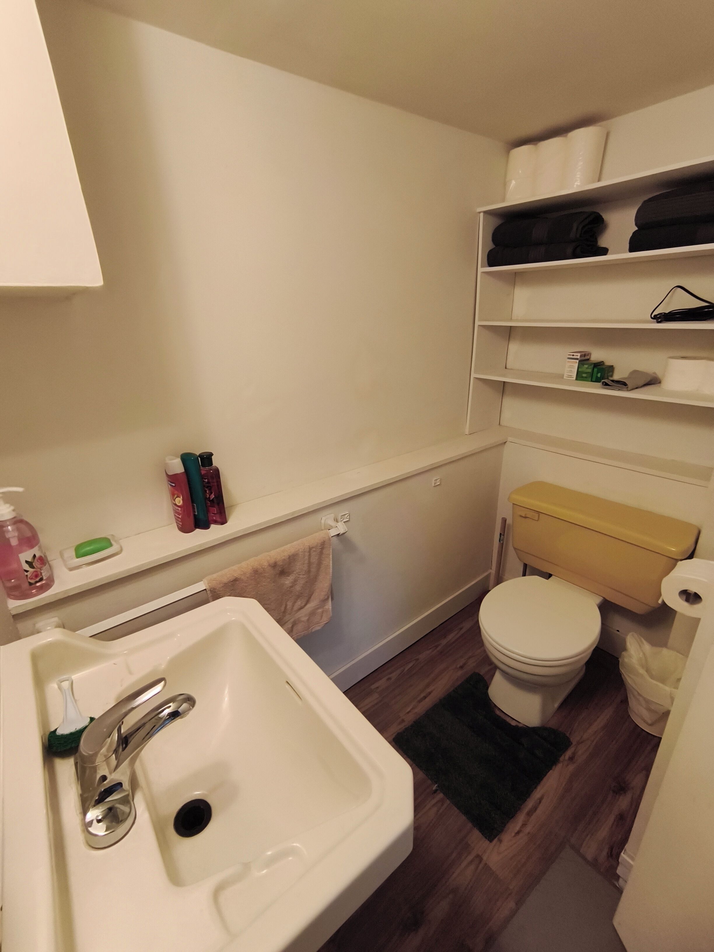 A bathroom with a sink, toilet, shelves with toiletries, and a towel rack.