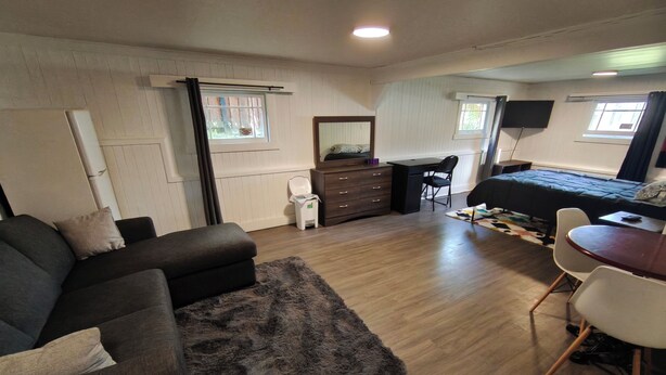 A room with a sofa, a desk, a chair, a bed, a TV, and a window. - East Vancouver Bachelor Basement Suite. Pet Friendly - No Fee. Next to Transit. (Vancouver)