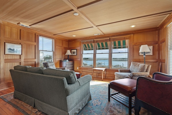 A cozy living room with a sofa, chairs, a small table, and a view of the water through large windows.