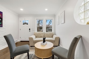 Een moderne woonkamer met een beige bank, twee grijze fauteuils, een houten salontafel en een katbeeldje.