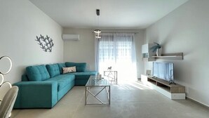 A modern living room with a teal sofa, a glass coffee table, a TV on a wooden stand, and a ceiling light. - Athenean Modern Escape near Marina Flisvos-E1 (Paleo Faliro)