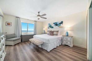 A bedroom with a bed, a bench, a nightstand, a dresser, a ceiling fan, and a window with a view. - Sandy Key 732 | Spacious Beachfront Condo | Pools, Hot Tub & Tennis | My Beach Getaways (Pensacola)