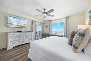 A hotel room with a bed, a ceiling fan, a television, a dresser, and a view of the ocean. - Sandy Key 732 | Spacious Beachfront Condo | Pools, Hot Tub & Tennis | My Beach Getaways (Pensacola)