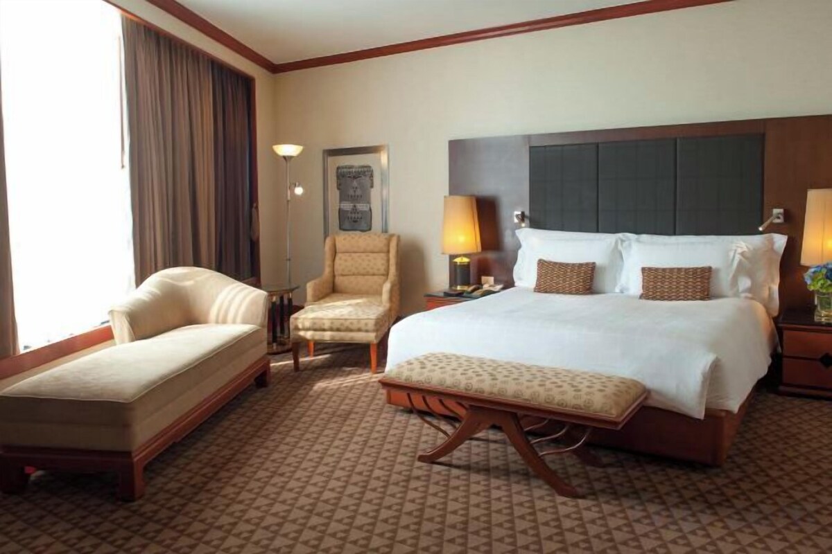 A hotel room with a large bed, a chair, a desk, and a lamp.