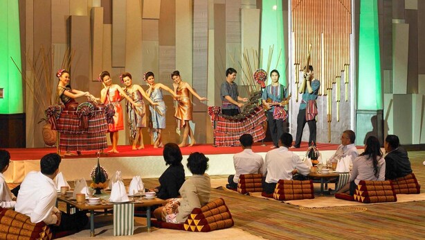 A stage with performers in traditional attire, seated audience, and a backdrop with vertical wooden slats. - The Heritage Grand Khon Kaen Hotel and Convention (Khon Kaen)