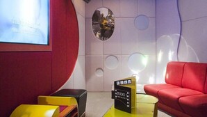 A modern room with a red sofa, a projector screen, a small table with a sign, and a unique wall design. - The Heritage Grand Khon Kaen Hotel and Convention (Khon Kaen)