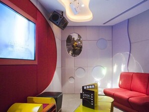 Une pièce moderne avec un canapé rouge, un écran de projection, une petite table avec un panneau et un décor mural original.
