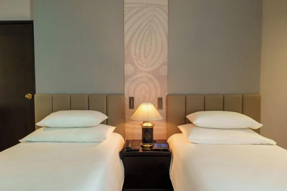 A hotel room with two beds, a nightstand with a lamp, and a patterned wall.
