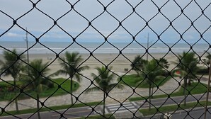 Ein stacheldrahtzaun mit Blick auf einen Strand, Palmen und eine Straße.