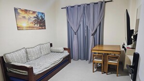 Ein Zimmer mit einer Couch, einem Tisch mit Stühlen, einem Fernseher und einem Bild an der Wand.