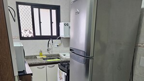 Eine kleine Küche mit einem Edelstahlkühlschrank, einem Gasherd und weißen Schränken.