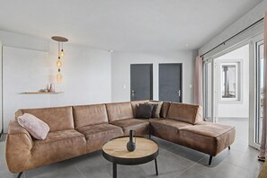 A modern living room with a brown leather sectional sofa, a round wooden coffee table, and pendant lighting. - AnochíLuz - Modern 3-bedroom apartment near Mambo beach (Willemstad)