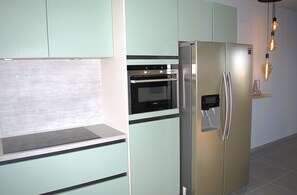 Eine Küche mit einem Edelstahlkühlschrank, einem Backofen und hellgrünen Schränken.