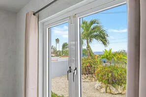 A sliding glass door leading to a balcony with a view of palm trees and a building. - AnochíLuz - Modern 3-bedroom apartment near Mambo beach (Willemstad)