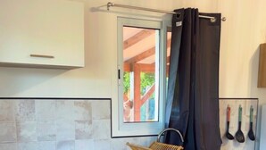 Une cuisine avec des meubles blancs, une cuisinière noire et une fenêtre avec un rideau.