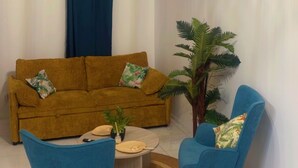 Un salon avec un canapé marron, deux fauteuils bleus, une table basse ronde, un luminaire suspendu, une horloge et un tableau accroché au mur.