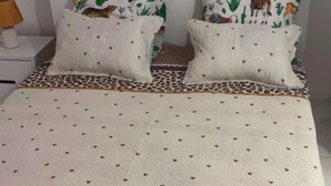 Un lit avec une couvre-lit à motifs et des coussins assortis, une table de chevet avec une lampe et une tête de lit blanche.