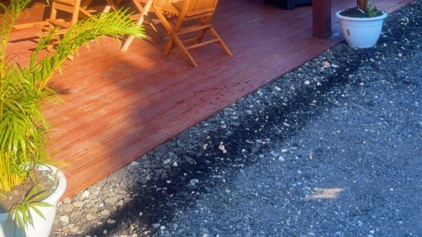 Une cabane en bois avec un toit rouge, une terrasse avec une table et des chaises, et un espace barbecue.