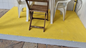 A yellow wall, a white tiled floor, a wooden table, and two white plastic chairs.