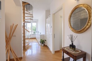 A modern interior with a spiral staircase, a wooden floor, a mirror, and a small table with a vase. - Vittoria Luxury Apartment (Treviso)