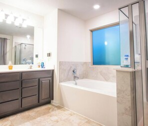 Un baño moderno con bañera, muebles oscuros, un espejo grande y una ventana con tonalidad azul.