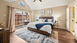 Ein Schlafzimmer mit Bett, Deckenventilator, Nachttisch, Lampe und Fenster mit Vorhängen.