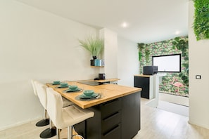 A modern kitchen with a wooden countertop, black cabinets, and a small island with seating. There is a plant on the wall and a decorative wall mural with tropical plants and a flamingo. - KOSTA HOMES - Duplex Apartment Near The Beach (Torremolinos)
