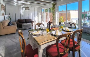 A dining area with a table set for four, surrounded by chairs with red cushions, a sofa, and a patterned ottoman.