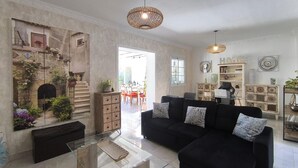 A living room with a black sofa, glass coffee table, decorative items, and a view into the dining area. - Cozy home in Guillena (Guillena)