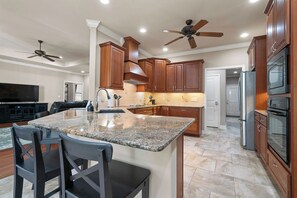 A modern kitchen with granite countertops, wooden cabinets, a central island with seating, and built-in appliances. - 4 Alabanza Retreat! Hot Spring Village near 4 Golf Courses (Hot Springs Village)
